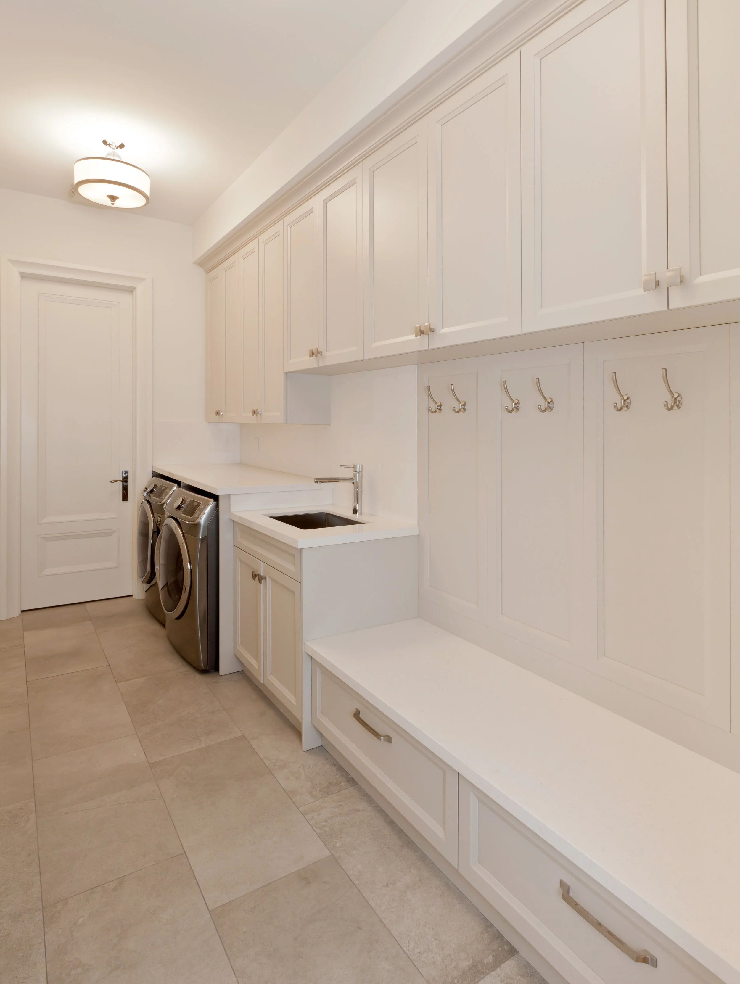 Salle de lavage avec armoires blanches, comptoir et banc intégré.